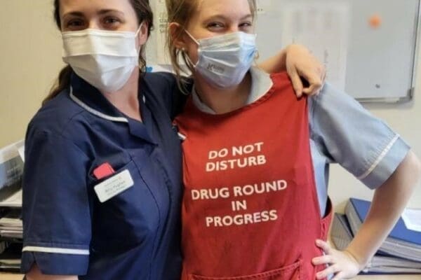 Two members of staff at Denham Manor standing next to each other, one of which is Katrina wearing a red apron as part of her CHAPS training