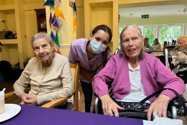 Two Denham Manor Care Home residents sitting at a purple table with their carer bending down between them
