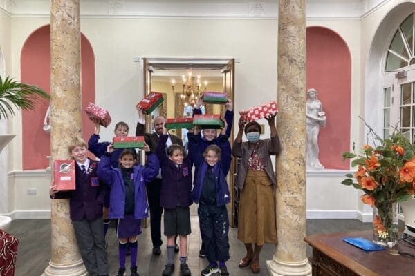School children lifting Christmas shoe boxes over their heads in celebration of their charitable efforts