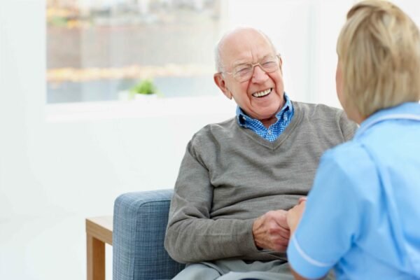 Happy elderly male patient talking with female nurse at home
